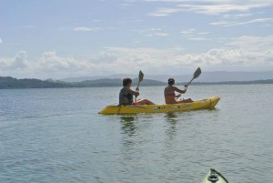 Two persons rowing in a double, yellow kayak in a bay.