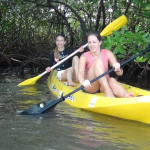 Two girls in a kayak paddling through mangroves