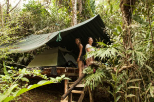 Two girls in front of a tent on a platform in jungle